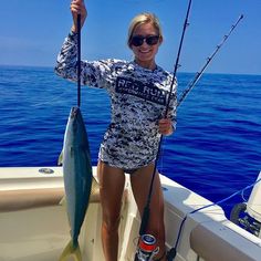 a woman holding two fish while standing on a boat in the ocean with it's fishing rod