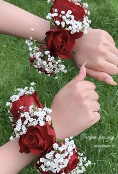 two hands are holding red roses and baby's breath flowers in their wristbands