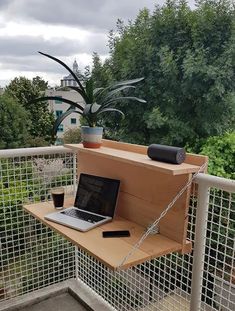 a laptop computer sitting on top of a wooden shelf next to a plant in a pot