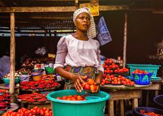 a woman standing in front of a table filled with tomatoes