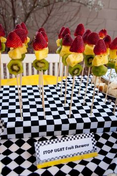 some strawberries and kiwis are on sticks in front of a checkered tablecloth