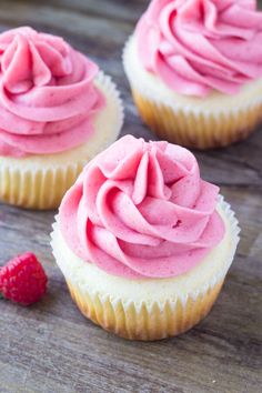 three cupcakes with pink frosting and a raspberry on the side