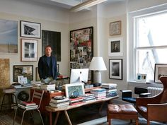 a man standing in front of a desk full of books and laptops with pictures on the wall behind him