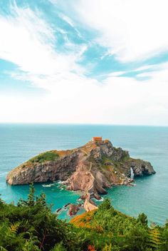 an island in the middle of the ocean surrounded by trees and rocks with a small house on top