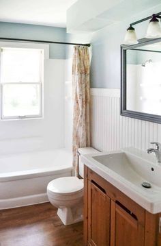 a white toilet sitting next to a bath tub under a bathroom mirror with a window