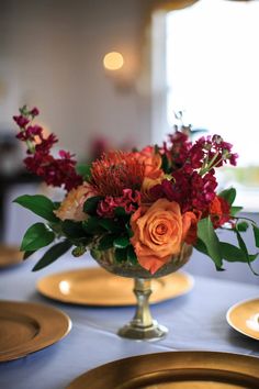 a vase filled with flowers sitting on top of a table next to gold plateware