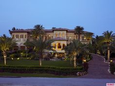 a large house with palm trees and landscaping in front of it at dusk or dawn