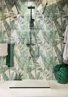 a bathroom with green leaves on the wall and a shower head in the middle, next to a towel rack