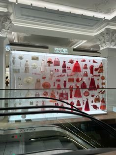 an escalator in front of a display case with dresses and purses on it