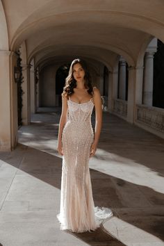 a woman in a long white dress standing on a stone walkway with arches behind her