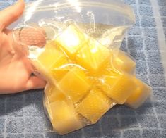 a hand holding a plastic bag filled with cubes of yellow food sitting on top of a blue towel