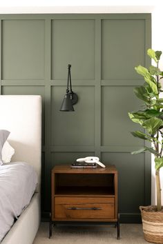 a bedroom with green paneled walls and a white bed in the corner next to a plant