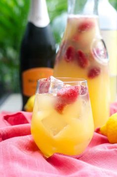 two glasses filled with lemonade and raspberries on top of a red cloth