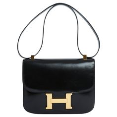 Hermès Constance model bag in smooth black "box" leather and gold metal, black leather interior with a zipped pocket and a patch pocket, large pocket on the back of the bag, black leather shoulder strap to wear single (shoulder, or cross body) or double (hand or shoulder), year 1969 or 1970. Width 23 cm x height 18 cm x depth 5 cm, double shoulder strap 52 cm or single 87 cm. The bag is vintage and the leather and metalwork show slight signs of use but it remains in excellent condition, chic, pr Black Hermes Bag, Vintage Hermes Bag, Hermes Purse, Kelly Bag, Cross Bag, Chanel Black, Black Box, Small Shoulder Bag, Hermes Bag