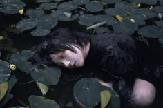 a woman is floating in the water with lily pads on her chest and black hair