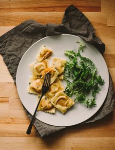 a white plate topped with ravioli and greens