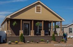 two people are standing in front of a small house with brown siding and stone pillars