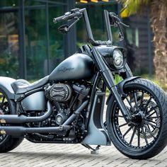 a black motorcycle parked on top of a brick road next to a palm tree in front of a building