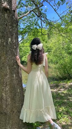 a girl in a dress standing next to a tree with her hands on the trunk