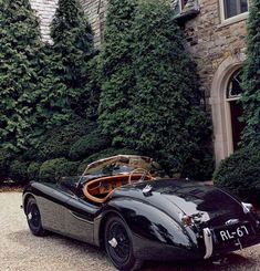 an old fashioned black sports car parked in front of a building with ivy covered trees