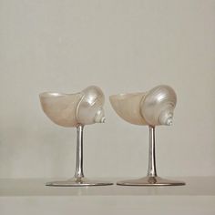 two glass vases sitting on top of a white table next to each other in front of a wall