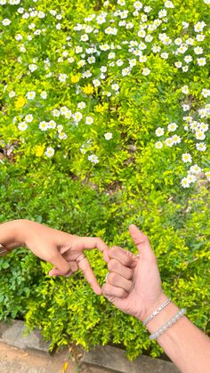 two people reaching out their hands to touch each other in front of some white and yellow flowers