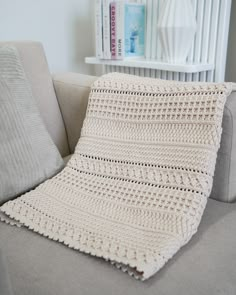 a white crocheted blanket sitting on top of a couch next to a book shelf