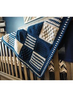 a crocheted blanket hanging from the side of a wooden rail in front of a blue wall