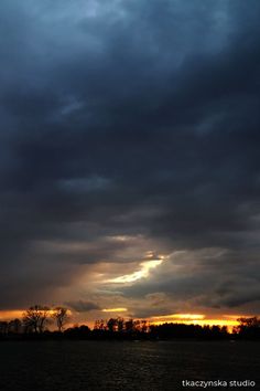 the sky is dark and cloudy as the sun sets in the distance behind some trees