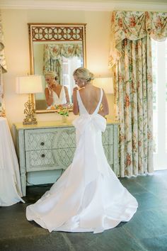 a woman standing in front of a mirror wearing a white dress