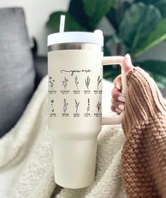 a person holding a coffee cup on top of a blanket with the names of plants printed on it