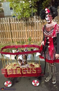 a woman dressed in costume standing next to a wagon filled with items that look like circus clowns