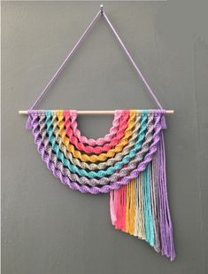 a multicolored crocheted wall hanging on a gray wall with a wooden stick