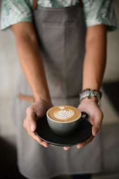 a person holding a plate with a cup of coffee on it in their hands and wearing an apron