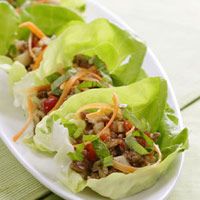 two lettuce wraps filled with meat and vegetables on a white plate next to a fork