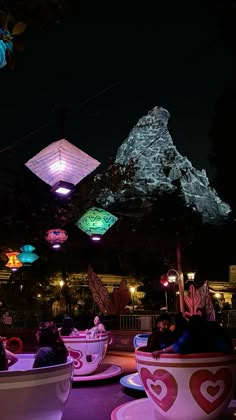 people are sitting in teacups with lights hanging from the ceiling above them at night