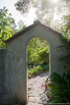 an arch in the side of a stone wall with trees and bushes around it on a sunny day