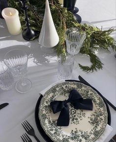 a table set with black and white plates, silverware, candles and greenery