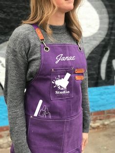 a woman standing in front of a graffiti wall wearing an apron with the words garage studio on it