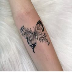 a black and white butterfly tattoo on the right arm, with flowers around its wings