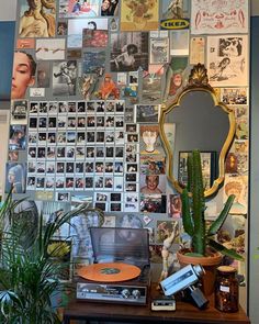 there is a wall covered with many pictures and plants on the table in front of it