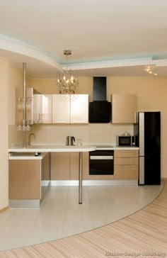 an empty kitchen with white counter tops and black appliances on the counters in front of a chandelier