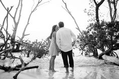 a man and woman standing in the water next to some tree branches, looking at each other