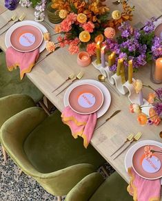 the table is set with pink and orange plates, place settings, candles, and flowers