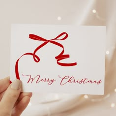 a person holding up a card with a red ribbon on it that says merry christmas