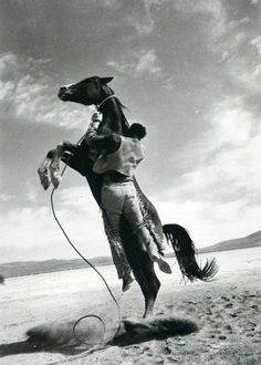 a man riding on the back of a horse across a desert field under a cloudy sky