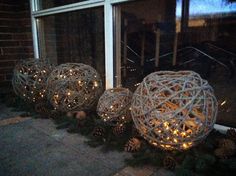 three balls with lights on them sitting in front of a window at night, next to pine cones