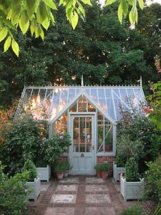 a small greenhouse with potted plants in front of it and lights on the door