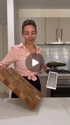 a woman standing in front of a kitchen counter holding a piece of wood next to an oven