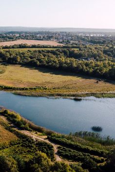 an aerial view of a lake surrounded by lush green fields and trees in the distance